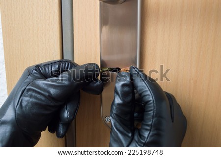 hands gloves of a thief open a security door of a house with a pick lock and tools