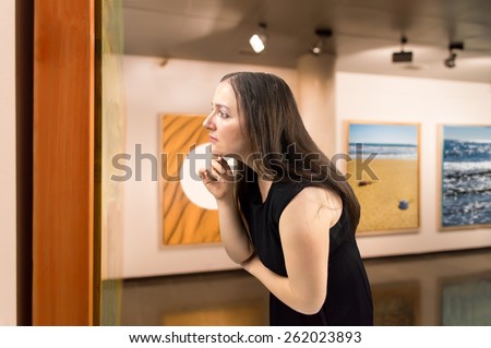 Woman closely scrutinizing a painting at an exhibition of the museum.Background photos are my property