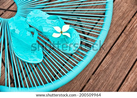 Turquoise blue garden chair and flip flops, wooden deck background