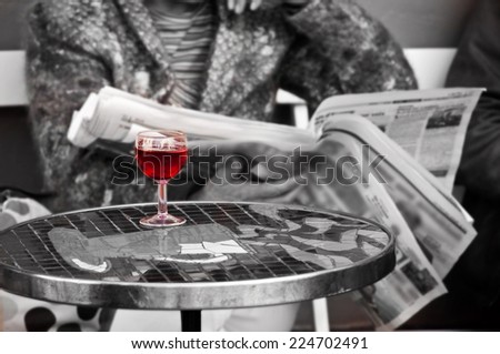 Close on a glass of red wine of a woman in a bar with a newspaper