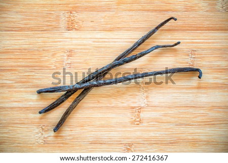 Three vanilla pods with a flower on wooden background