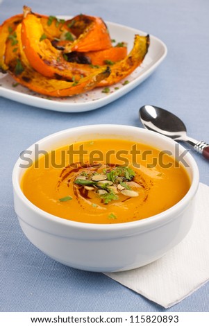 Bowl with pumpkin soup and roasted pumpkins on background