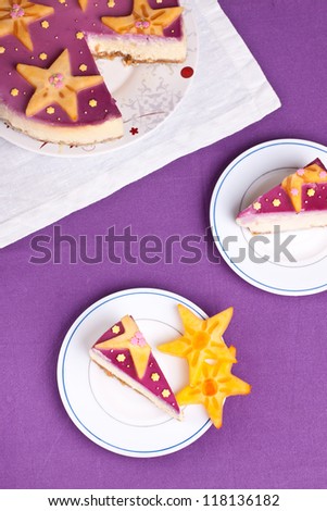 Two slices of delicious white chocolate cheese cake and a cake on purple background