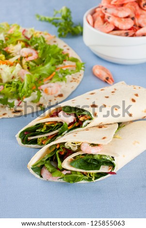 Wrap sandwich with shrimps and lettuce with boiled shrimps in a bowl on background