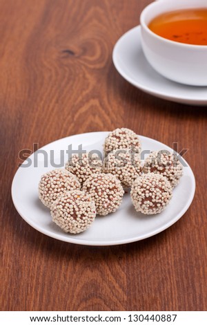 Chocolate truffles on small plate with cup of black tea on background