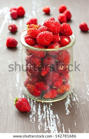Wild strawberries in a glass jar with some berries on background, shallow depth of field