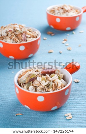 Three orange bowls full of muesli with various nuts