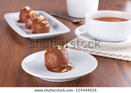 Chocolate truffle decorated with almond crumbs with some truffles and a cup of tea on background, selective focus