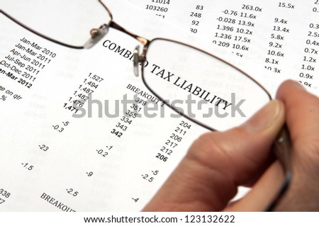 Hand holding magnifying glasses showing the words tax liability on financial paper