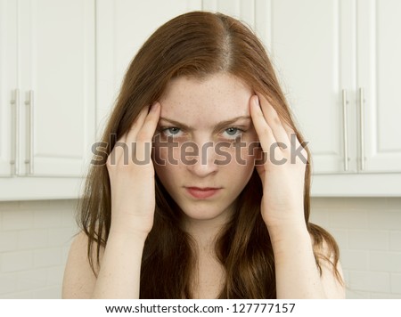 Stressed young woman in kitchen with hands to head