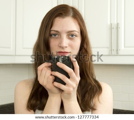 Contented young woman with cup of tea or coffee in the kitchen