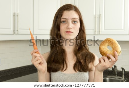 Young woman holds a carrot and a bagel in a choice between low glycemic index food or low GI food (carrot)  and high glycemic index food (bagel)