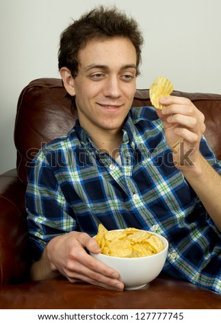 Young man on couch eating potato chips