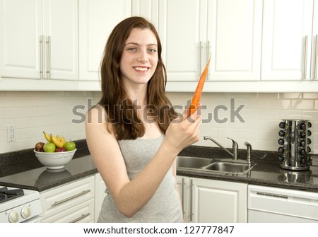 Young woman holds  carrot which has a low glycemic index or  low GI  in kitchen with white cabinets
