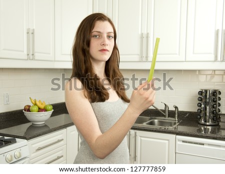 Young woman holds  celery  which has a low glycemic index or  low GI  in kitchen with white cabinets
