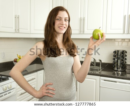 Young woman holds green apple which has a low glycemic index or  low GI  in kitchen with white cabinets