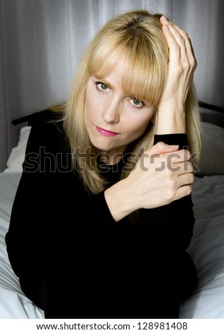 Depressed woman sits on bed with hands to head