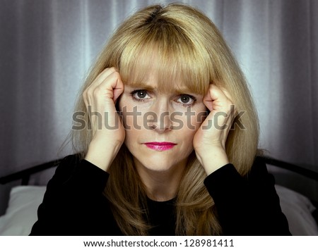 Depressed woman sits on bed with hands on face