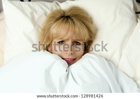 Woman pulling blanket to her face in bed with expression of fear