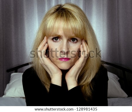 Depressed woman sits on bed with hands on face