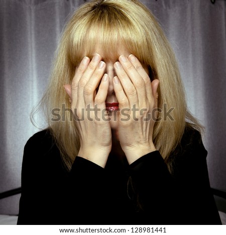 Depressed woman sits on bed with hands covering face