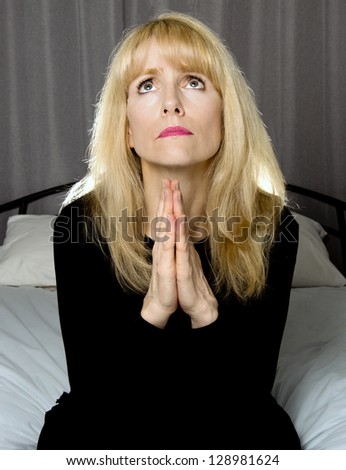 Depressed woman sits on bed praying