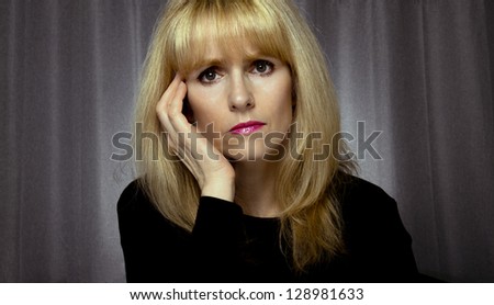 Depressed woman sits on bed with hand on face