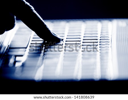 Concept photo in high contrast black and white of hacker\'s single finger on keyboard