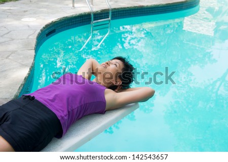 As Asian woman has a relaxing moment on the diving board of her swimming pool