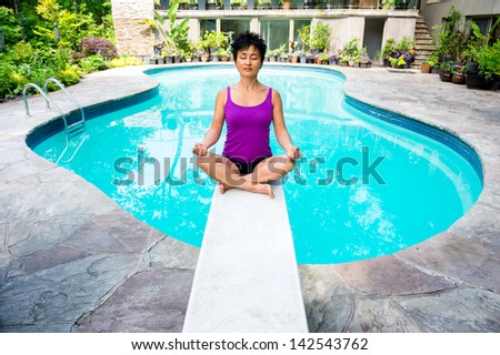 As Asian woman has a Zen moment on the diving board of her swimming pool