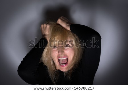 Crazy, angry woman pulling hair out and screaming for mental health concept