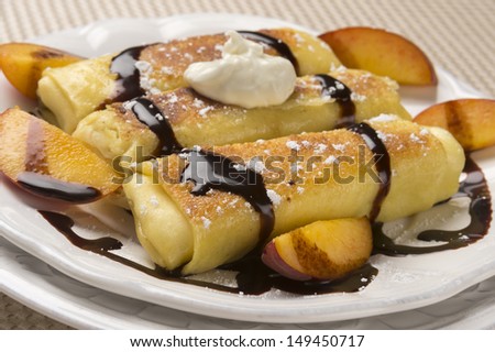 Traditional Jewish food cheese blitzes with whipped cream, peaches and chocolate sauce in closeup