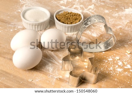 ingredients for cookies on wooden cutting board with eggs, heart and man shaped cutters, white and brown sugar