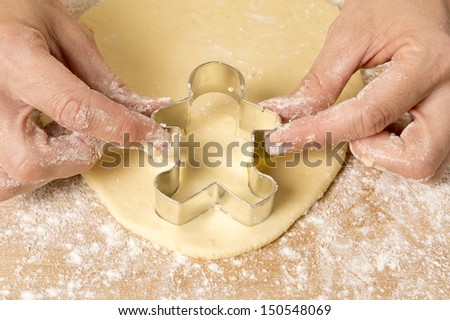Hands pushing man shaped cookie cutter into dough shot from above