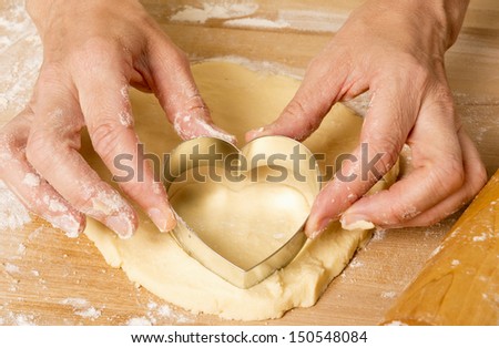 Hands pressing heart shaped cookie cutter into dough
