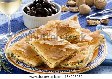 Spanakopita, Greek spinach pie with feta cheese and filo party on on plate with Greek white wine, olives and walnuts