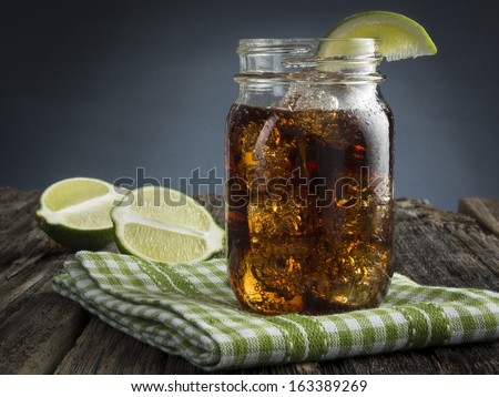 Cuba Libre or rum and cola drink with ice and lime in mason jar