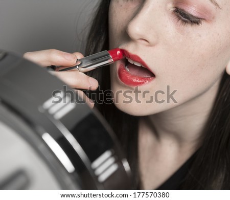 A young woman applies red lipstick in makeup mirror