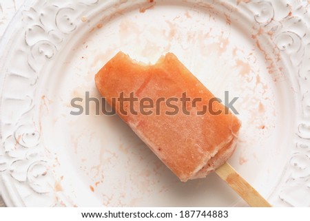 Strawberry, orange, pineapple, mango fruit popsicle with bite out of it shot from above