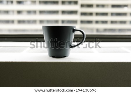 Coffee cup sits on window ledge in office building with view of another building
