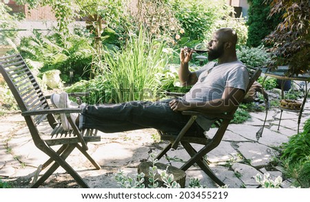 African American man relaxing in the backyard garden drinking a glass of red wine
