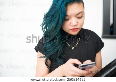 Asian woman with blue hair texting on smartphone