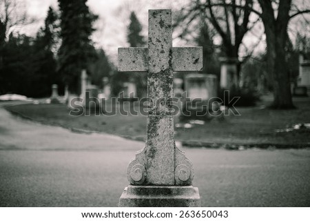 Corroded Cross grave marker in cemetery on gloomy day in black and white
