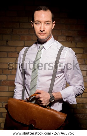 Portrait of a confident businessman and briefcase with high contrast lighting wearing sunglasses. With beard stubble.