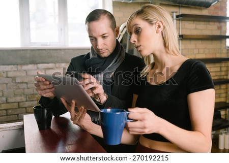 Entrepreneur couple discuss business in their office while looking at tablet computer