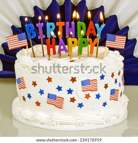 American Patriotic Themed Birthday Cake With Lit Candles And Patriotic Banner In Background Focus On Foreground