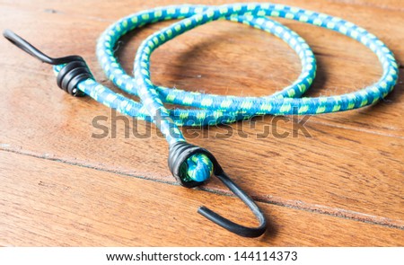 Blue elastic rope with metal hooks on wood background