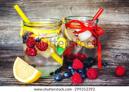 Lemonade with summer berries in glass jar with handle on wooden background