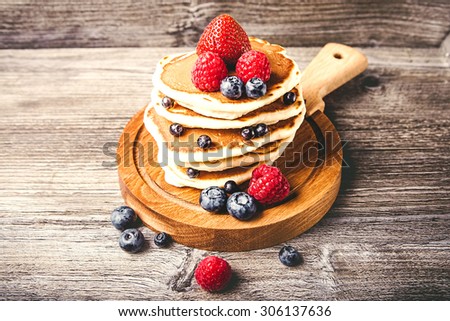 Pancakes with fresh summer berries and powdered sugar on wooden background