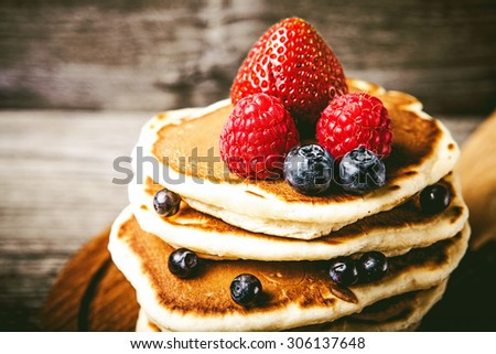 Pancakes with fresh summer berries and powdered sugar on wooden background